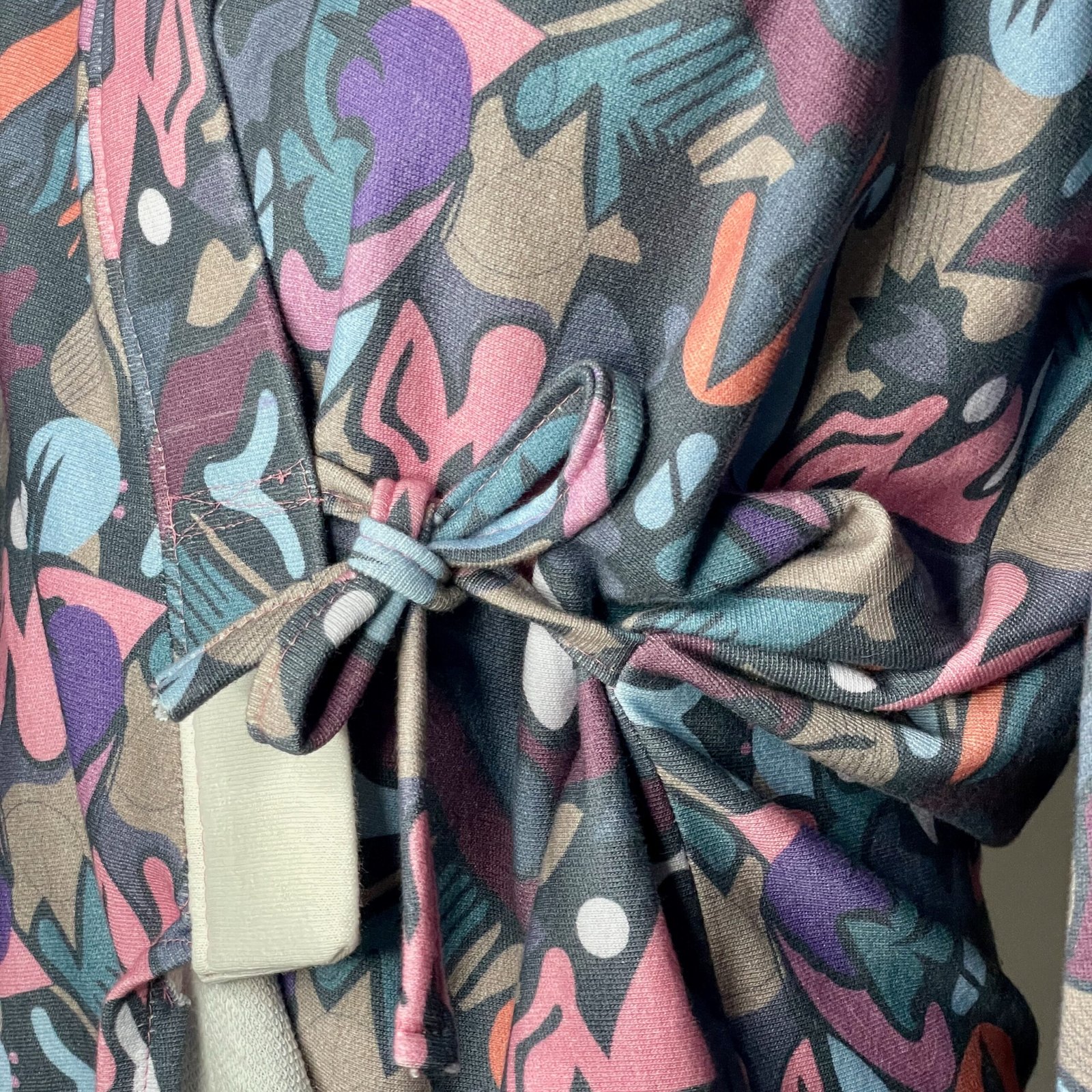 img 0866 Détail d'une veste pour femme avec un imprimé coloré, nouée avec des lanières. Parfaite pour ajouter une touche de style à votre tenue ! Motif Graffiti multicolore