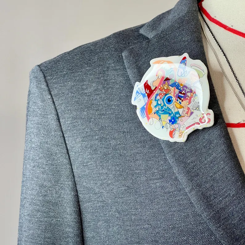 il 794xn.7018168522 qnur.jpg Broche graffiti colorée inspirée de Paris 2024, épinglée au col d’un costume gris sur un mannequin de couture masculin. Création buuBoo.
