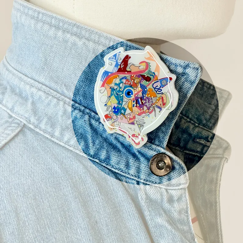 il 794xn.7066148193 kq9y.jpg Broche graffiti colorée inspirée de Paris 2024, épinglée au col relevé d’une chemise en jean bleu. Création buuBoo.