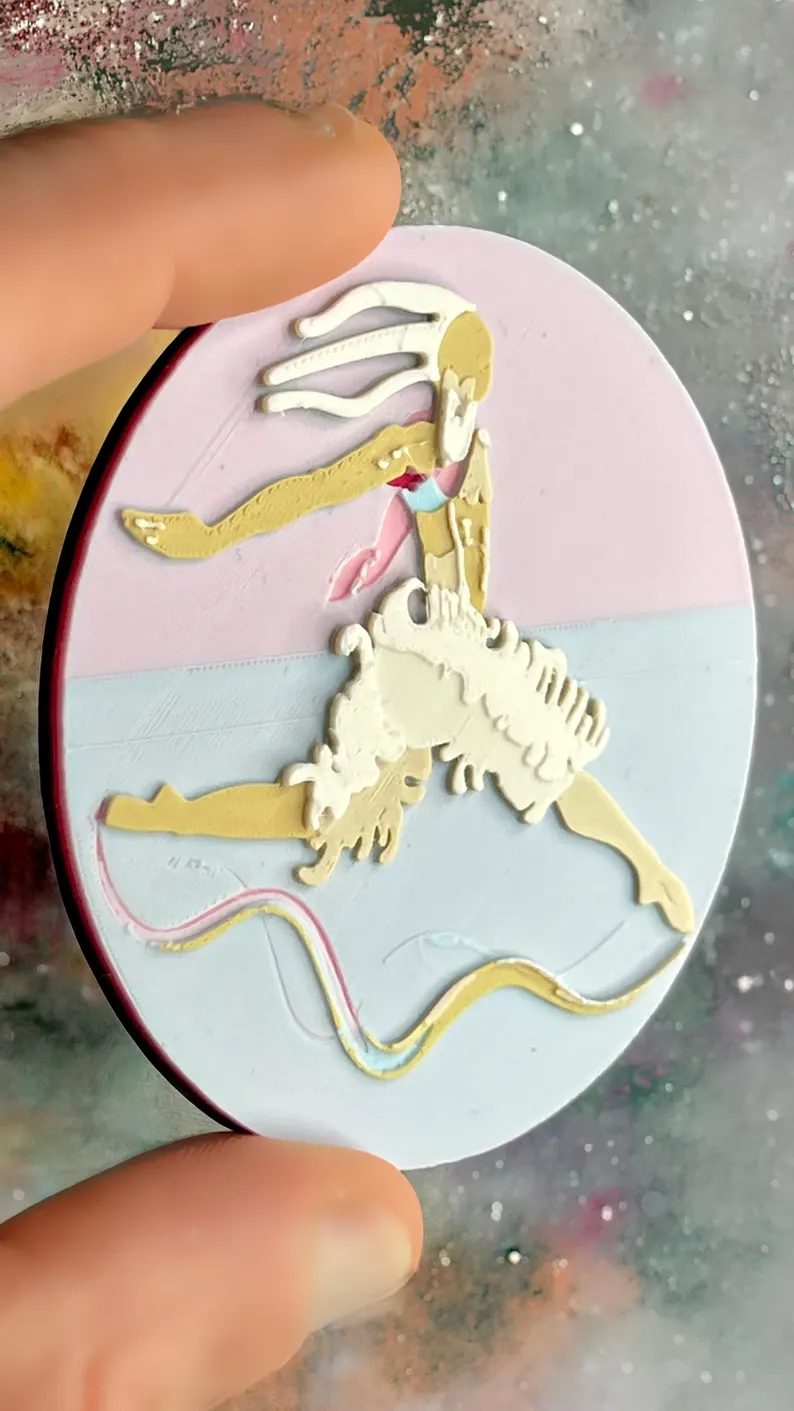 il 794xn.8344674705 9ex7.jpg Broche ronde Danseur-Cygne présentée en main, relief imprimé en 3D avec palette pastel effet nuage, personnage aux dégradés beige et blanc et fond rose bleu doux. Marque buuBoo.