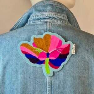 Patch coquelicot au vent brodé au point de chaînette, fixé sur le haut d’une chemise en jean épais, légèrement sous le col. Marque buuBoo.
